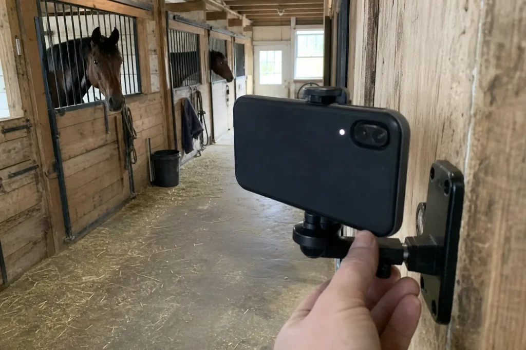 En hand justerar en mobilkamera monterad vid stallgång, i samband med att travtränare utreds efter att ha slagit häst i hu...